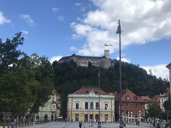 Een foto van het kasteel van Ljubljana met daaronder de gele gevel van Academia Philharmonicorum op het congresplein