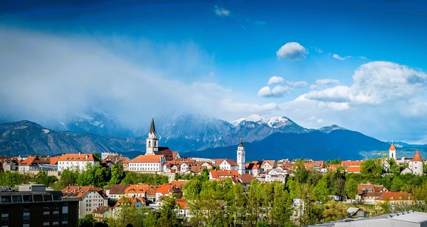 Het uitzicht van de stad Kranj met onder meer de klokkentoren van Sint Cantianus & op de achtergrond de besneeuwde bergtoppen