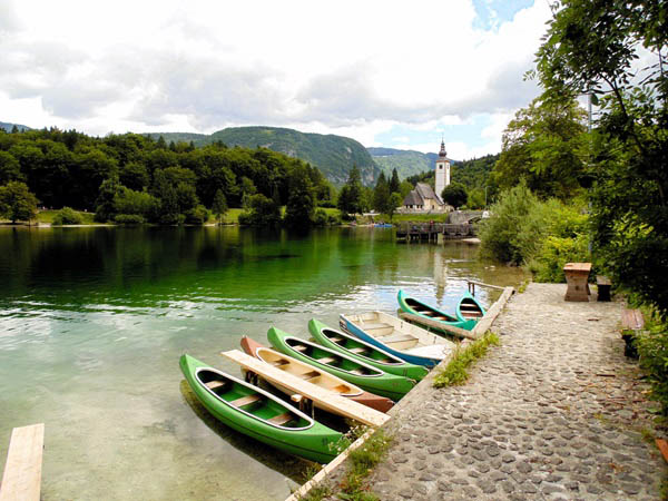 Een blik op het meer van Bohinj met op de voorgrond groene kajakboten